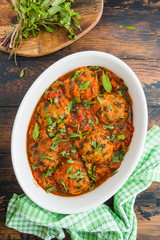 Chopped fish cutlets in spicy tomato sauce with fresh mint. White dish on wooden rustic table, top view