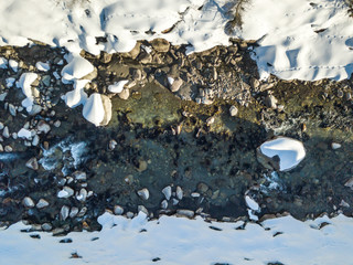 Aerial view of snow covered stones in river flowing through winter landscape from above.