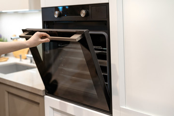 Woman hand opening built-in oven in white kitchen cabinet