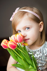 cute little blonde girl of three years with peach tulips close-up, smiling, look into the camera, vertical photo