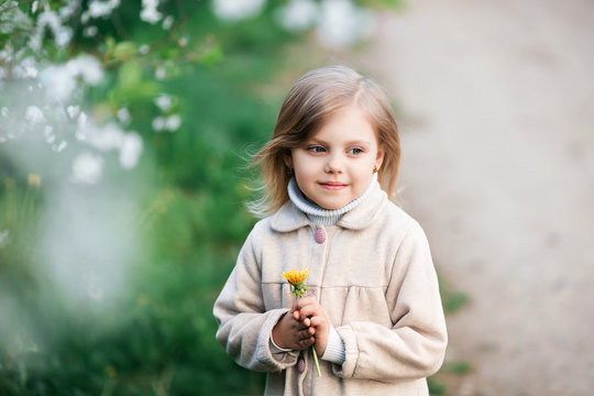Photo of a happy child, a small blonde girl in nature, on a walk, near a cherry blossoming, spring garden, in a coat