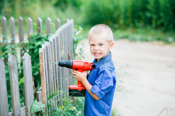 little blond boy of five years old with blue eyes on the street with a screwdriver / drill