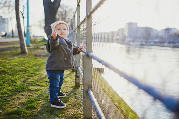 One year old girl standing next to metal fence in park