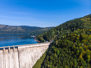 Obraz premium Aerial scenic view of a dam constructed on a beautiful valley in mountains. water storage reservoir. road with beautiful views for travel and holidays. lake Lzvorul Muntelui, Romania.