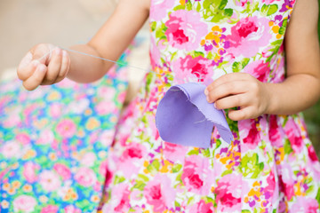 small child 4 years old (girl) in cotton dress sewing needle (hand) of the purple cloth on a background of a beautiful calico cloth outdoor largly