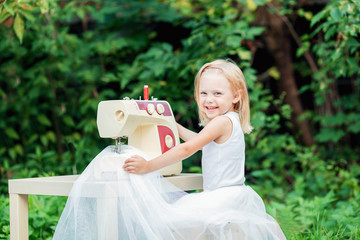 blond child 4 years (a little girl) near the sewing machine, scribbling on a white cloth