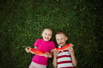 cute happy children boy and girl 6-7 years old eating watermelon outdoors