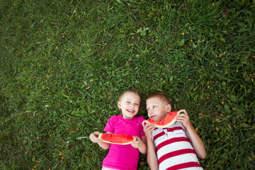 Fototapeta na wymiar cute happy children boy and girl 6-7 years old eating watermelon outdoors