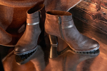 A pair of women's suede boots on a bronze reflective floor on the background of burlap and wooden boards. Warm creative lighting.