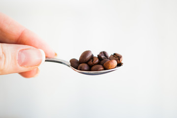 Coffee beans in the spoon on a white ground