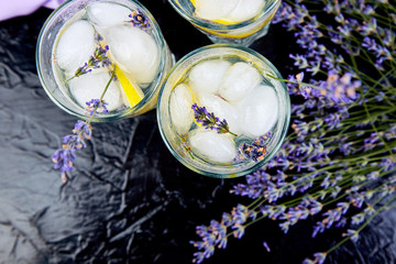 Lavender lemonade with lemon and ice on black background.