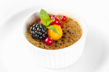 Dessert crème brulee with red currants, blackberries, mint and winter cherry on a white background