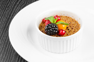 Dessert crème brulee with red currants, blackberries, mint and winter cherry on a white background