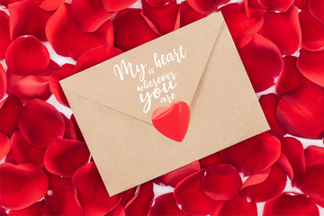 top view of envelope with "my heart is wherever you are" lettering, heart and red rose petals on background, st valentines day concept