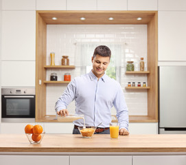 Young man in a shirt pouring milk into a cereal bowl for breakfast in a modern kitchen