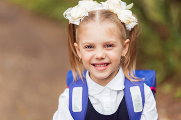portrait of a blond schoolgirl first-graders in school uniform with a knapsack, happy girl laughing