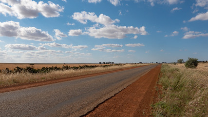 Typical Australian Outback Road, red sand, blue sky and Cumulus Clouds.