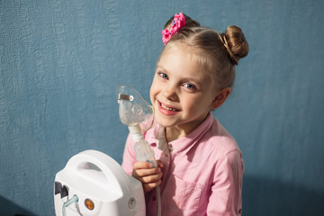 a little pretty blonde girl 5 - 6 years old in pink, breathes a compression nebulizer (inhaler) through a mask for lung disease, bronchitis and whooping cough, picture on a blue background...