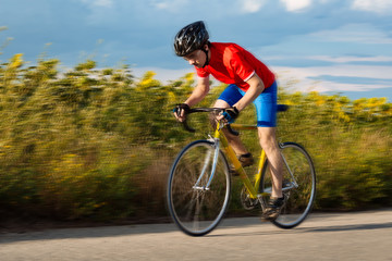 A cyclist rides on a road bike quickly along fields of sunflowers.