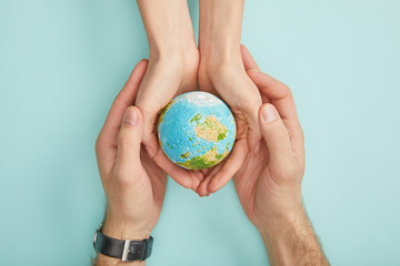 top view of man and woman holding planet model on turquoise background, earth day concept