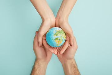 top view of man and woman holding planet model on turquoise background, earth day concept
