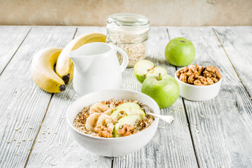 Healthy breakfast oatmeal with nuts ad fruits - apple, banana, walnuts, With milk on wooden background copy space