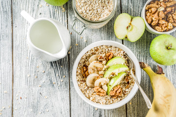 Healthy breakfast oatmeal with nuts ad fruits - apple, banana, walnuts, With milk on wooden background copy space