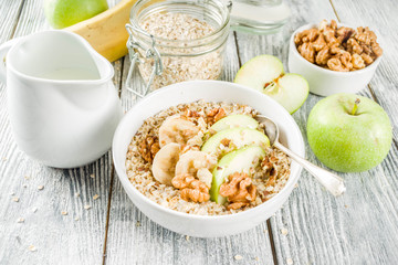 Healthy breakfast oatmeal with nuts ad fruits - apple, banana, walnuts, With milk on wooden background copy space