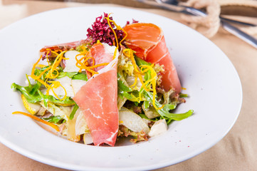 Close up Green Salad with prosciutto and pears in white plate close up. Served restaurant table. Selective focus, copy space.