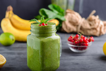 Healthy green spinach smoothie in a jar mug decorated with mint and red currant berries with ingridients on the black wooden table. Selective focus. Detox concept.