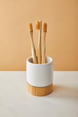brown bamboo toothbrushes in holder on white table and beige background
