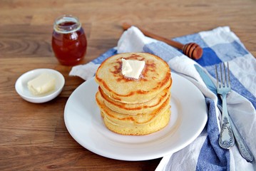 Cornmeal pancakes on a white plate. Served with butter and honey or maple syrup.