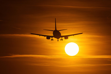 Fototapeta na wymiar Silhouette of an air plane near to the sun with beautiful red clouds in background