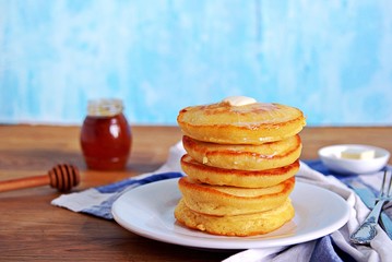 Cornmeal pancakes on a white plate. Served with butter and honey or maple syrup.