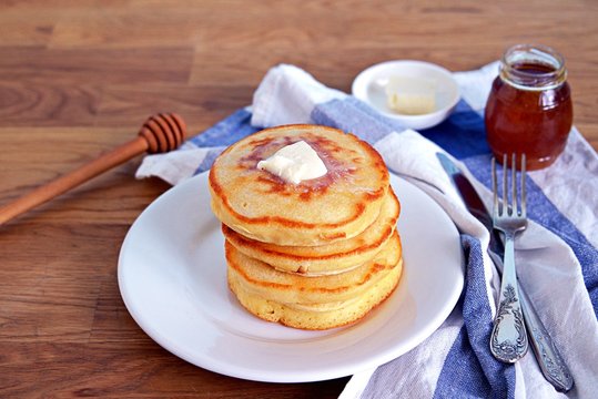 Cornmeal pancakes on a white plate. Served with butter and honey or maple syrup.