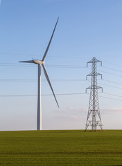 Wind turbine and electricity pylon in green field on blue sky