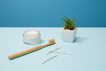 bamboo toothbrush, cosmetic cream and plant in pot on table and blue background