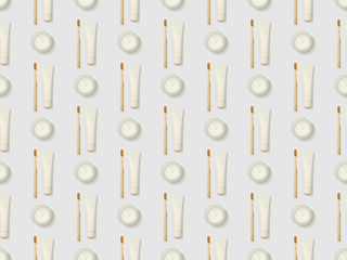 vertically bamboo toothbrushes, toothpaste in tube and cosmetic cream on grey background, seamless background pattern