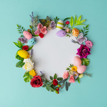 Easter wreath made of colorful spring flowers, leaves and easter eggs. Natural round frame layout with paper card. Flat lay.
