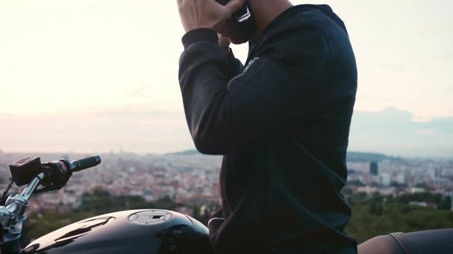 Parts of a cool motorbike Handsome moto biker guy just arrived and park by slide stand to his destination of beautiful view to Barcelona cityscape Taking off helmet and enjoying moment with his own