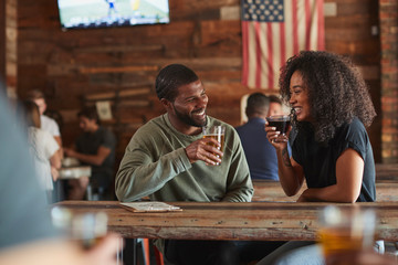 Young Couple Meeting In Sports Bar Enjoying Drink Before Game
