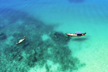 View from above, stunning aerial view of two traditional longtail boats floating on a turquoise and clear sea. Tropical beach with white sand, Freedom beach, Phuket, Thailand.