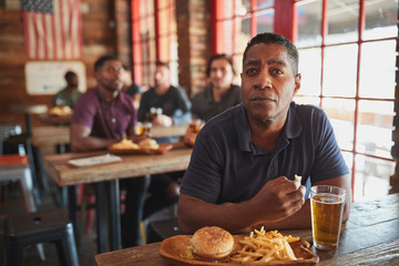 Man Watching Game On Screen In Sports Bar Eating Burger And Fries