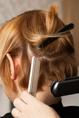 Fototapeta premium Hairstylist curl short hair with flat iron