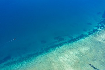 View from above, aerial view of a boat sailing near a stunning barrier reef with beautiful shades of blue and turquoise sea. West coast of Phuket, Thailand.