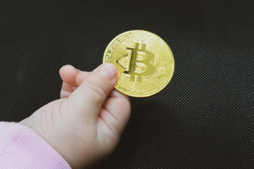 Child holds bitcoin coin in hand