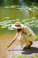 beautiful woman in summer hat and white dress near a pond