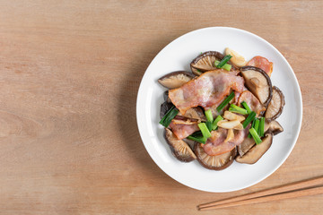 top view of stir fried shiitake mushroom and bacon with soy sauce in a ceramic dish on wooden table. homemade style food concept.