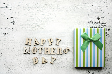 Happy mother's day. Wooden alphabet and Packaging. Blue and green stripes. Congratulations holiday mom. Copy space. Vintage crack background. Gift striped box with bow. Letters on a white background.