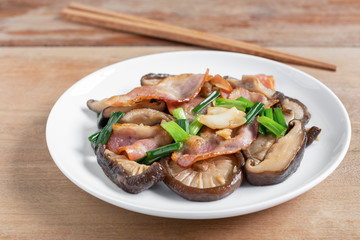 stir fried shiitake mushroom and bacon with soy sauce in a ceramic dish on wooden table, close up. homemade style food concept.